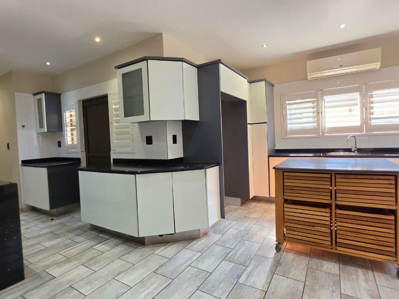 Modern kitchen featuring two-tone cabinetry, dark stone countertops, tiled flooring, and integrated lighting, offering a clean and functional workspace.