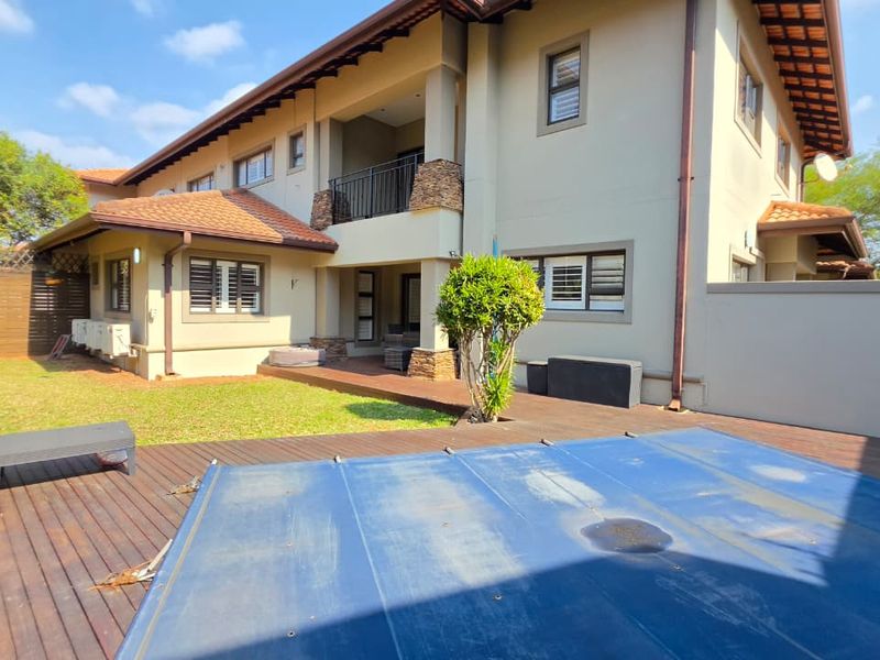 Rear exterior view of the duet property featuring a swimming pool with cover, wooden decking, and a covered balcony with stone-clad pillars.