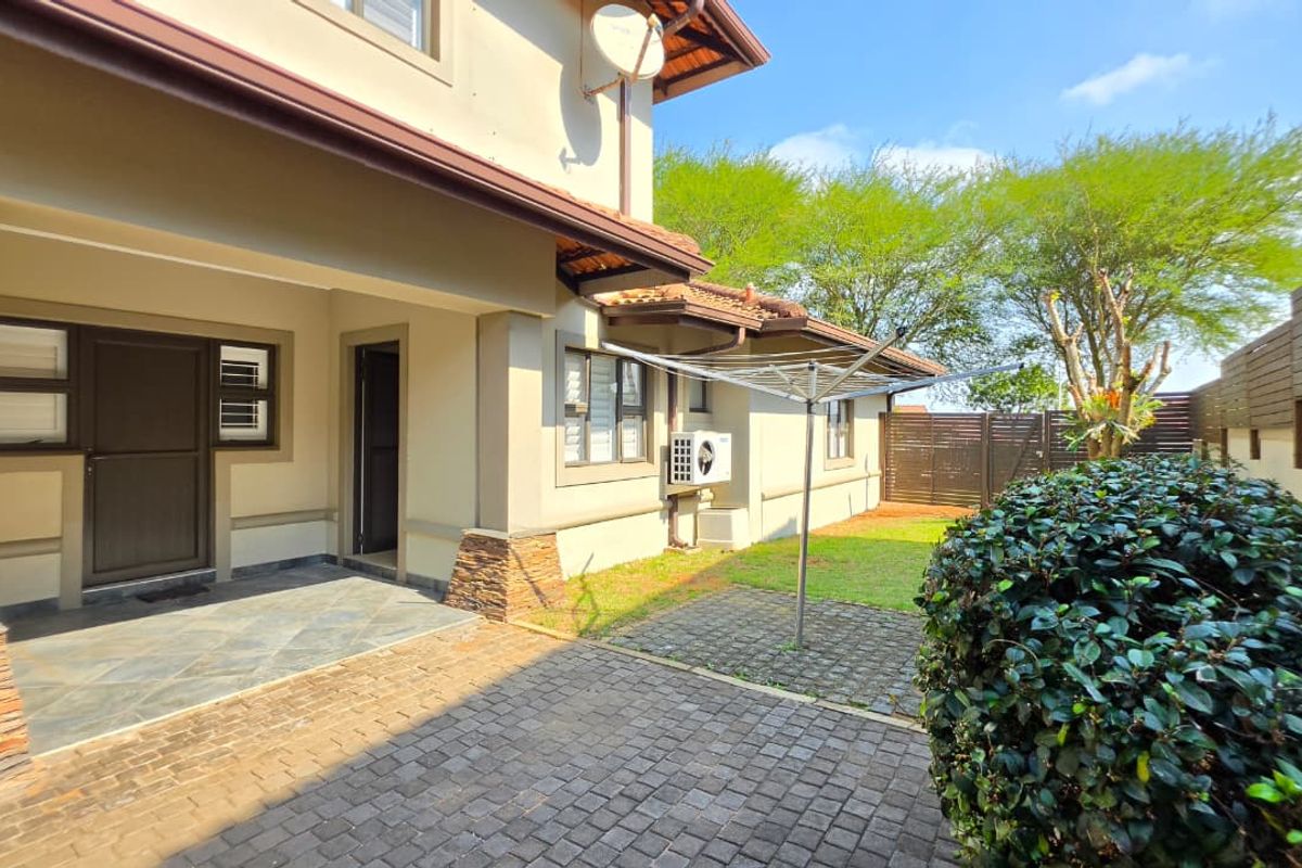 Rear exterior view of the duet property featuring a paved patio area, stone-clad pillars, and a private garden space with boundary fencing.