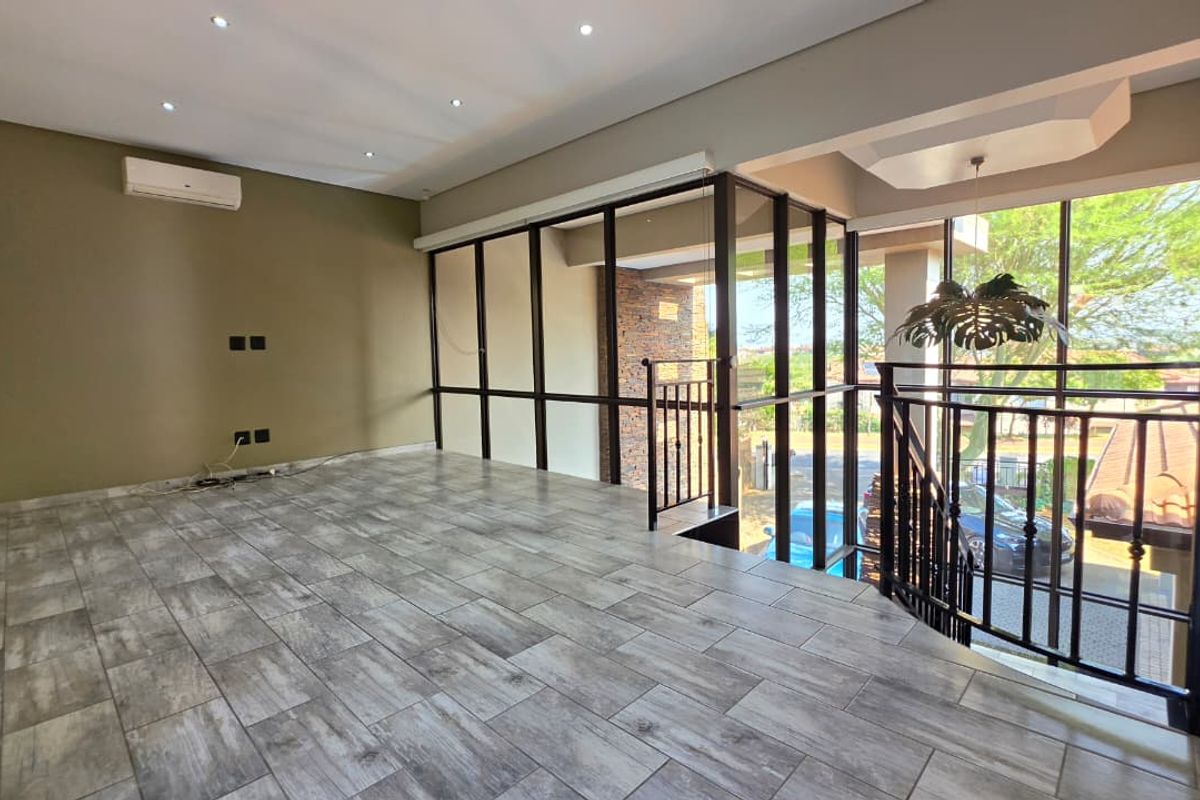 Spacious, light-filled living area featuring modern tiled flooring, recessed downlights, air conditioning, and a metal balustrade overlooking the staircase.