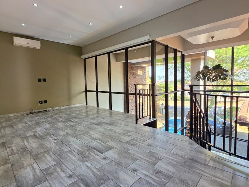 Spacious, light-filled living area featuring modern tiled flooring, recessed downlights, air conditioning, and a metal balustrade overlooking the staircase.