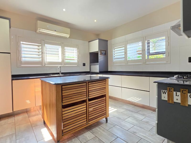 Modern kitchen featuring sleek cabinetry, stone countertops, a gas hob, integrated extractor, and plantation shutters, offering a bright and functional culinary space.