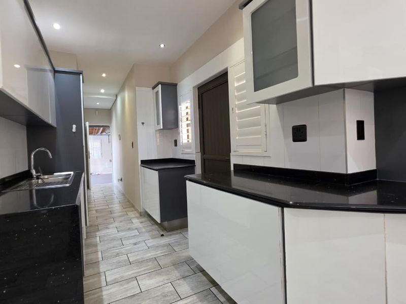 Modern kitchen featuring high-gloss cabinetry, contrasting black granite countertops, stainless steel sink, and contemporary tiled flooring with recessed lighting.