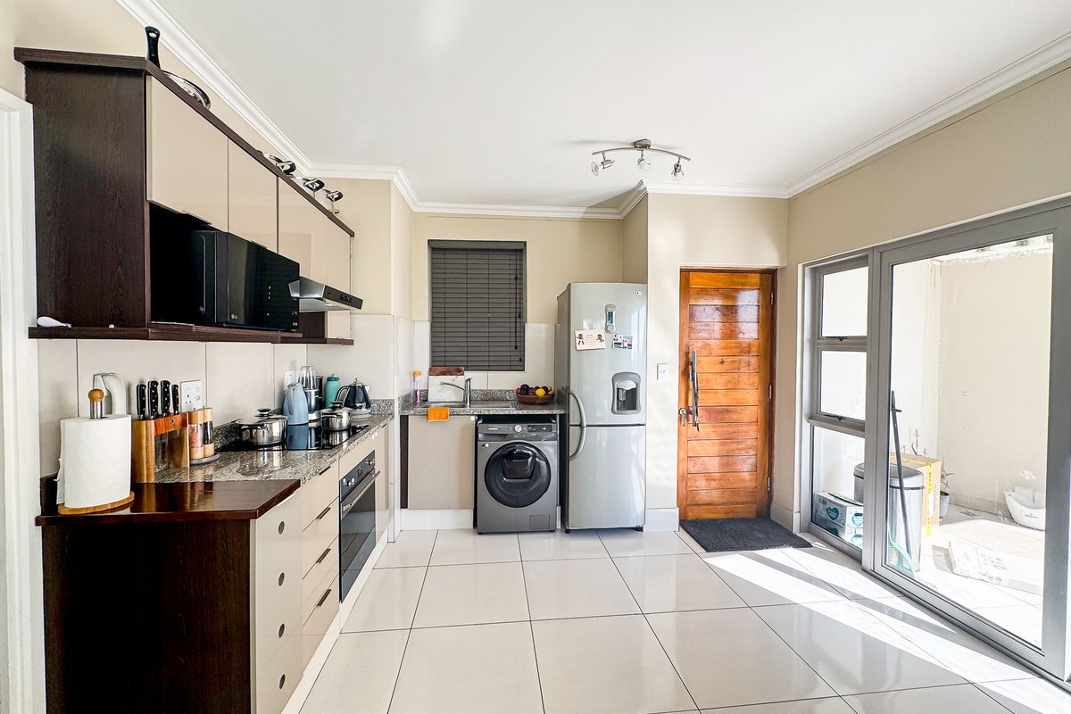 Modern kitchen featuring granite countertops, built-in oven, hob, extractor fan, and tiled flooring with direct access to an outdoor patio area.