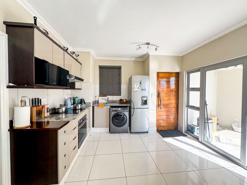 Modern kitchen featuring granite countertops, built-in oven, hob, extractor fan, and tiled flooring with direct access to an outdoor patio area.
