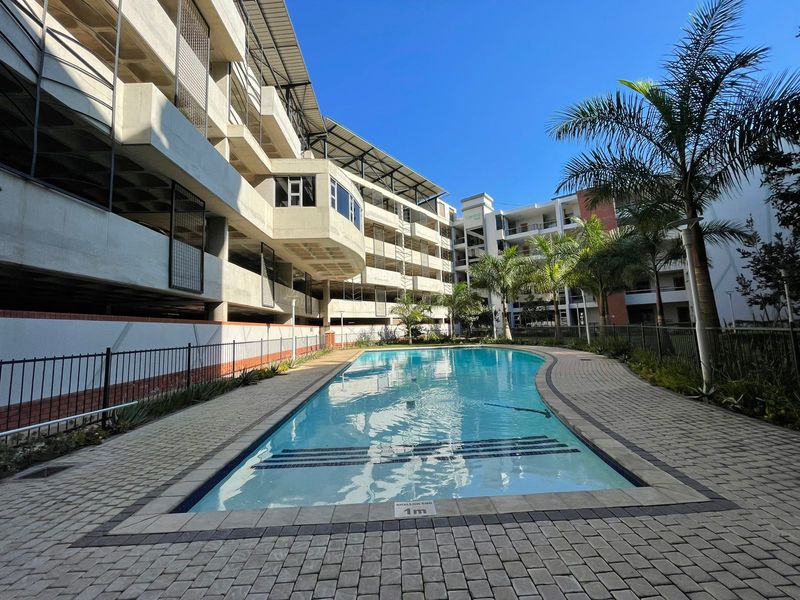 A well-maintained communal swimming pool area featuring paved surrounds and modern multi-story apartment building architecture.