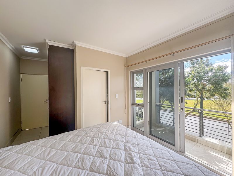 Bright bedroom featuring built-in cupboards, tiled flooring, and large sliding glass doors opening onto a private balcony with garden views.