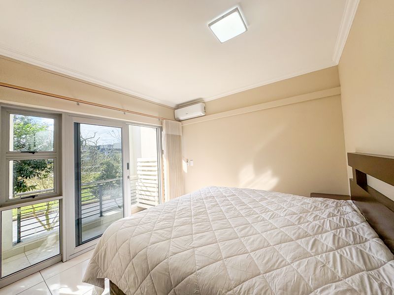 A bright bedroom featuring tiled flooring, a wall-mounted air conditioning unit, and a sliding glass door providing access to an outdoor balcony.