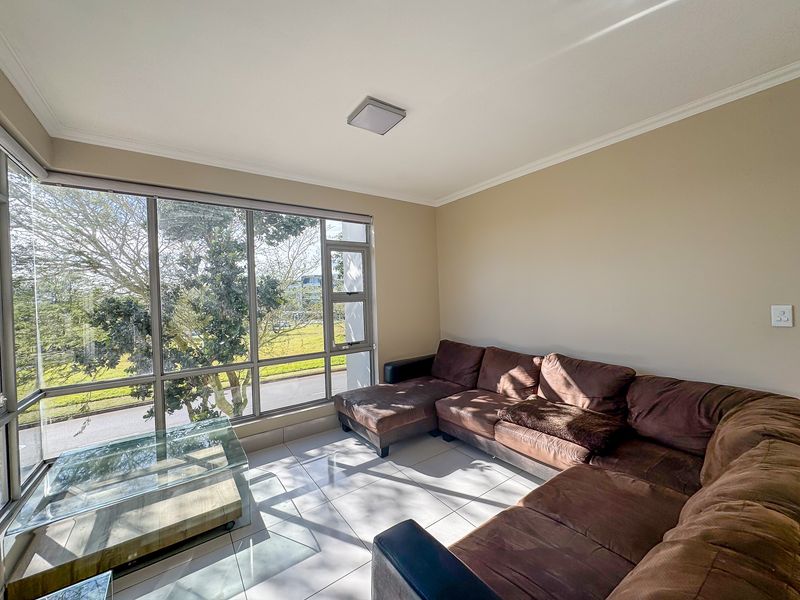 A bright living room featuring large floor-to-ceiling windows that provide ample natural light and views of the surrounding greenery.