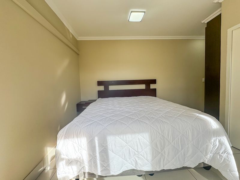 A bedroom featuring tiled flooring, built-in cupboards, and ceiling cornicing, providing a functional and neutral living space.