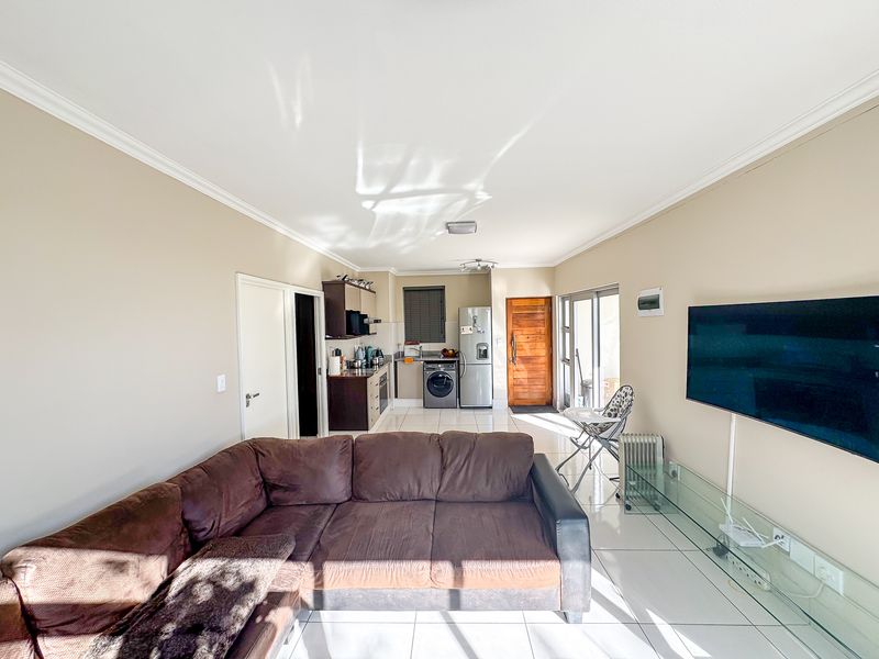 Open-plan living area featuring tiled floors, a compact kitchen with built-in cabinetry, and direct access to an outdoor space through sliding glass doors.