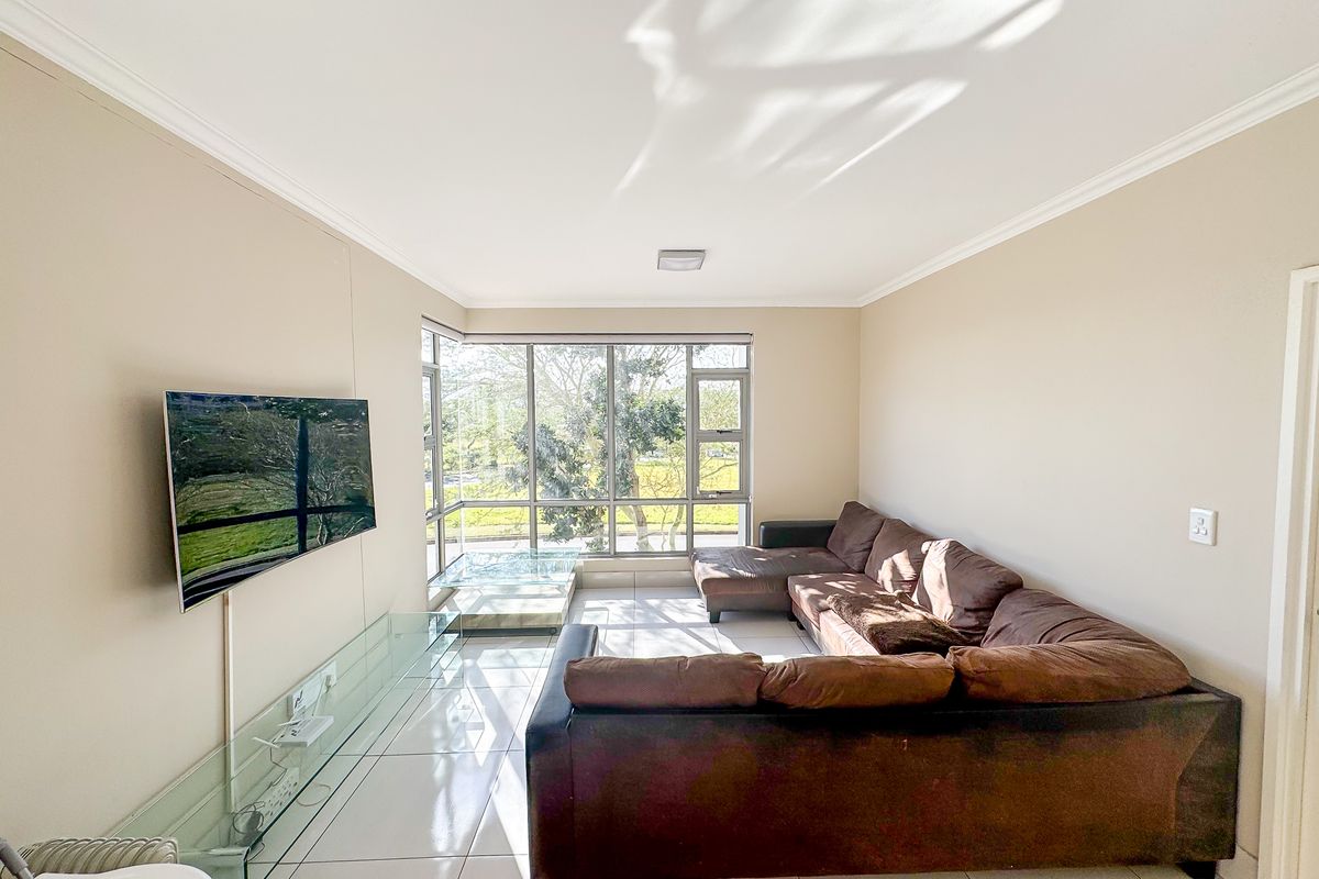 A bright and spacious living room featuring large corner windows that provide ample natural light and tiled flooring throughout.