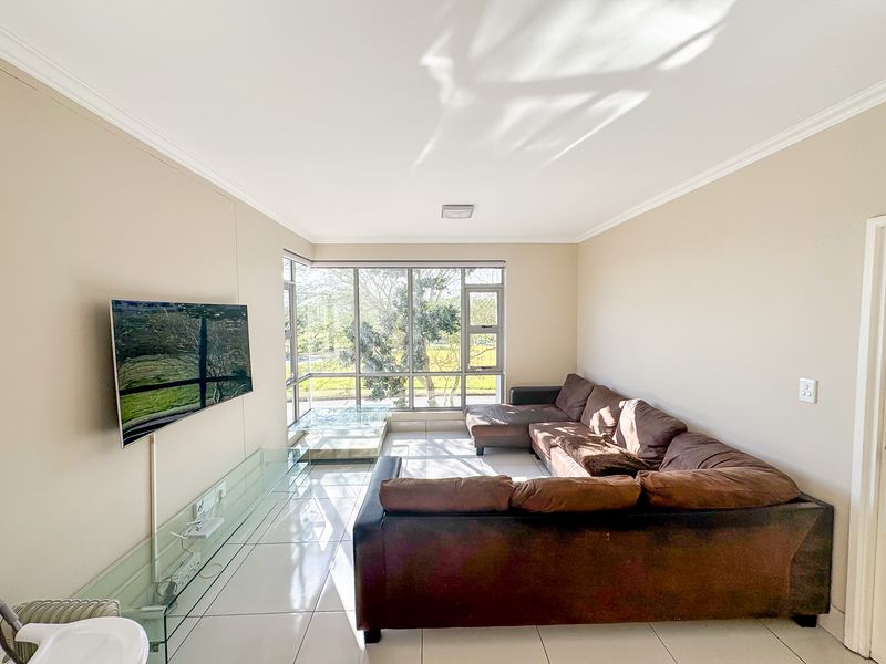 A bright and spacious living room featuring large corner windows that provide ample natural light and tiled flooring throughout.