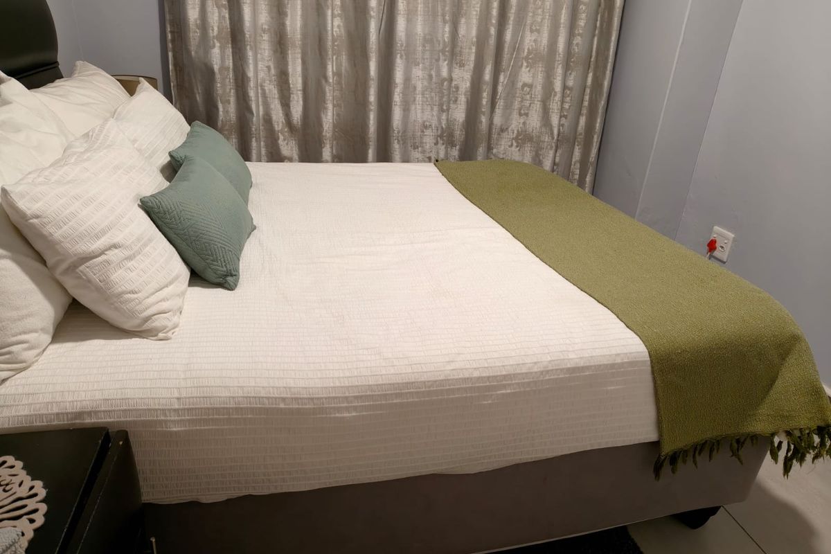 A bedroom featuring neutral wall tones, tiled flooring, and a window dressed with curtains.