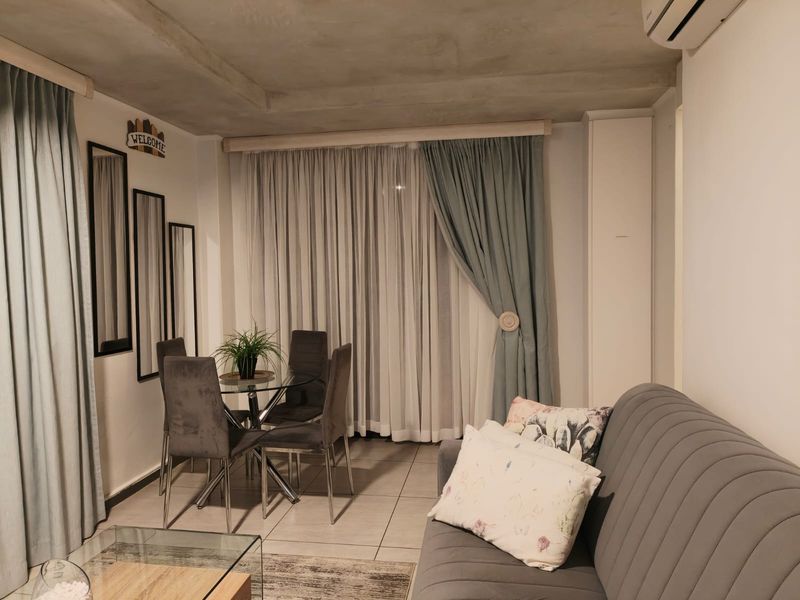An open-plan living and dining area featuring tiled floors, an exposed concrete ceiling, and a wall-mounted air conditioning unit.