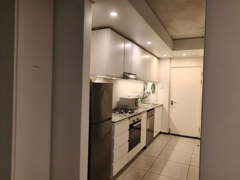 A modern, compact kitchen featuring white cabinetry, built-in oven and gas hob, stainless steel sink, and tiled flooring with recessed lighting.