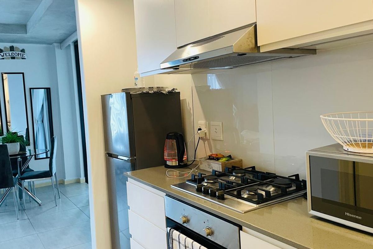Modern kitchen featuring white cabinetry, stone countertops, a gas hob, built-in oven, and a glass splashback, seamlessly flowing into the adjacent dining area.
