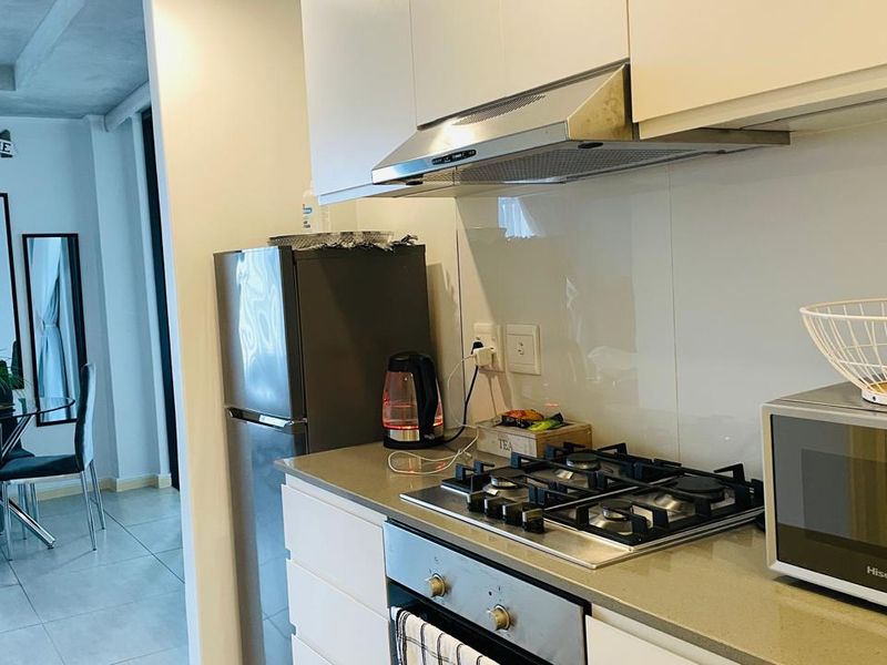 Modern kitchen featuring white cabinetry, stone countertops, a gas hob, built-in oven, and a glass splashback, seamlessly flowing into the adjacent dining area.