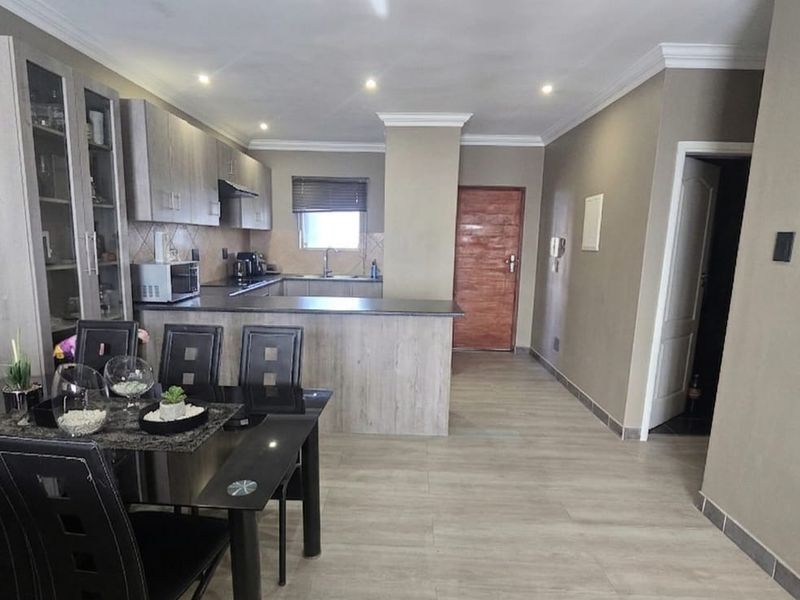 Open-plan living and kitchen area featuring modern cabinetry, laminate flooring, recessed lighting, and a functional breakfast bar layout.