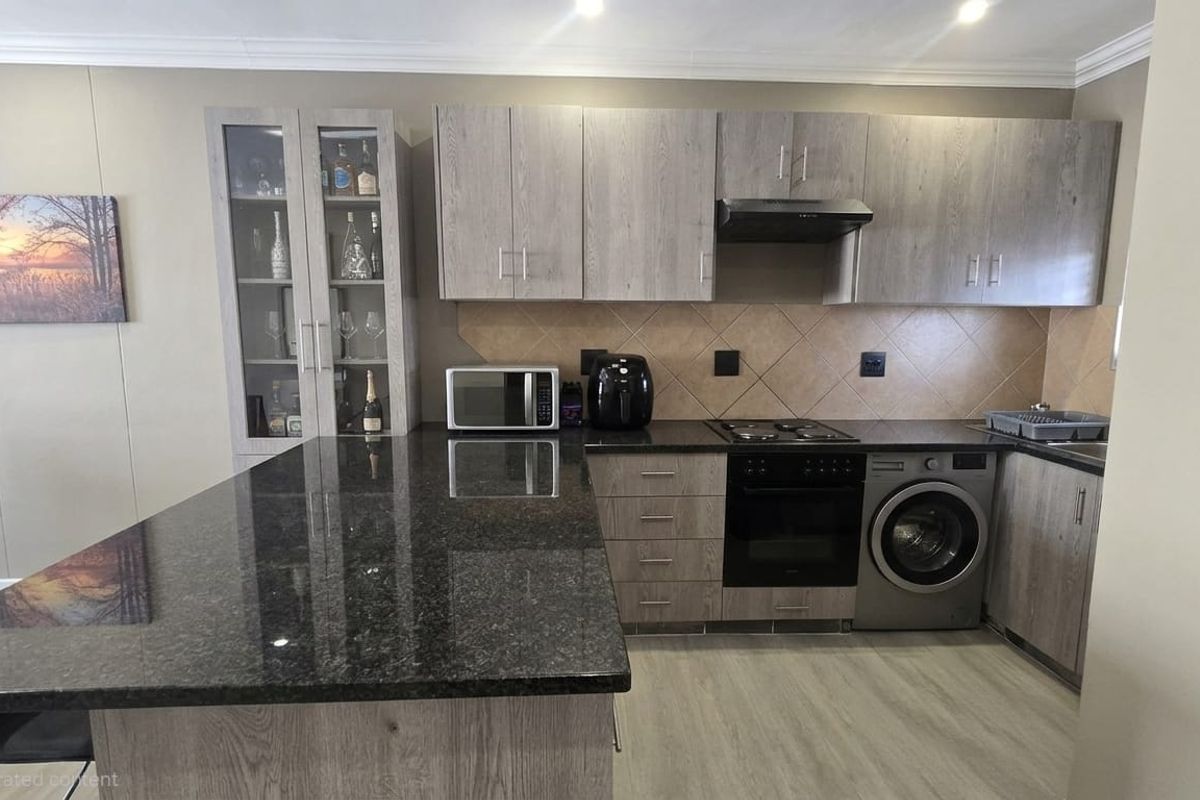 Modern kitchen featuring grey wood-grain cabinetry, dark granite countertops, a tiled backsplash, and integrated appliances including an oven, hob, and washing machine.