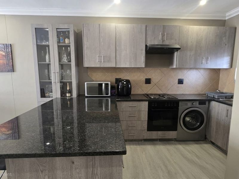 Modern kitchen featuring grey wood-grain cabinetry, dark granite countertops, a tiled backsplash, and integrated appliances including an oven, hob, and washing machine.