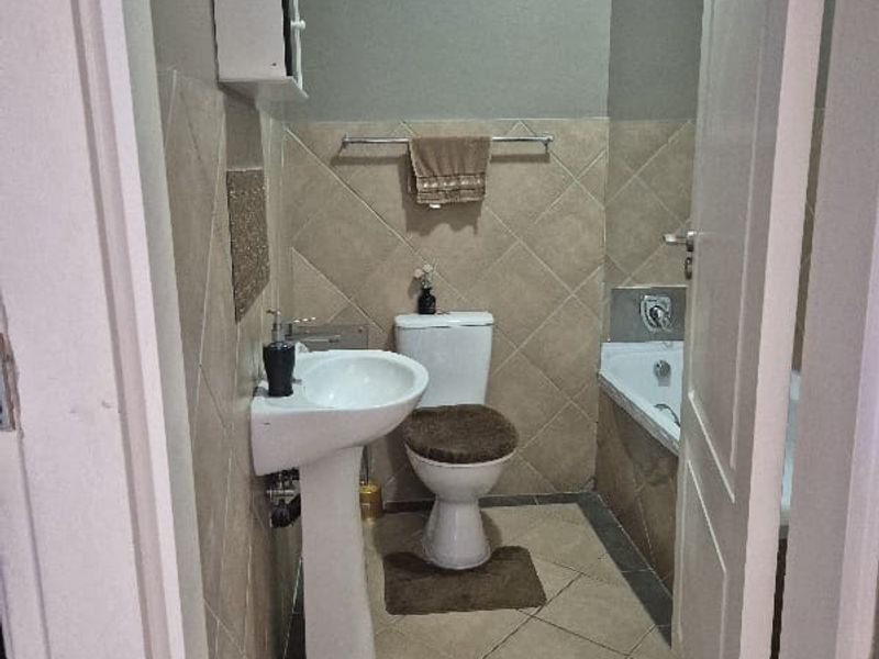 A functional bathroom featuring a pedestal basin, toilet, and bathtub with neutral tiled finishes and wall-mounted storage.