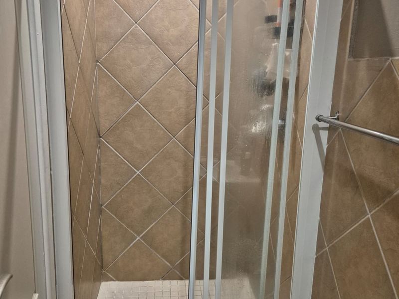 A functional shower stall featuring diamond-patterned wall tiles, a white tiled floor, and a sliding glass door enclosure.