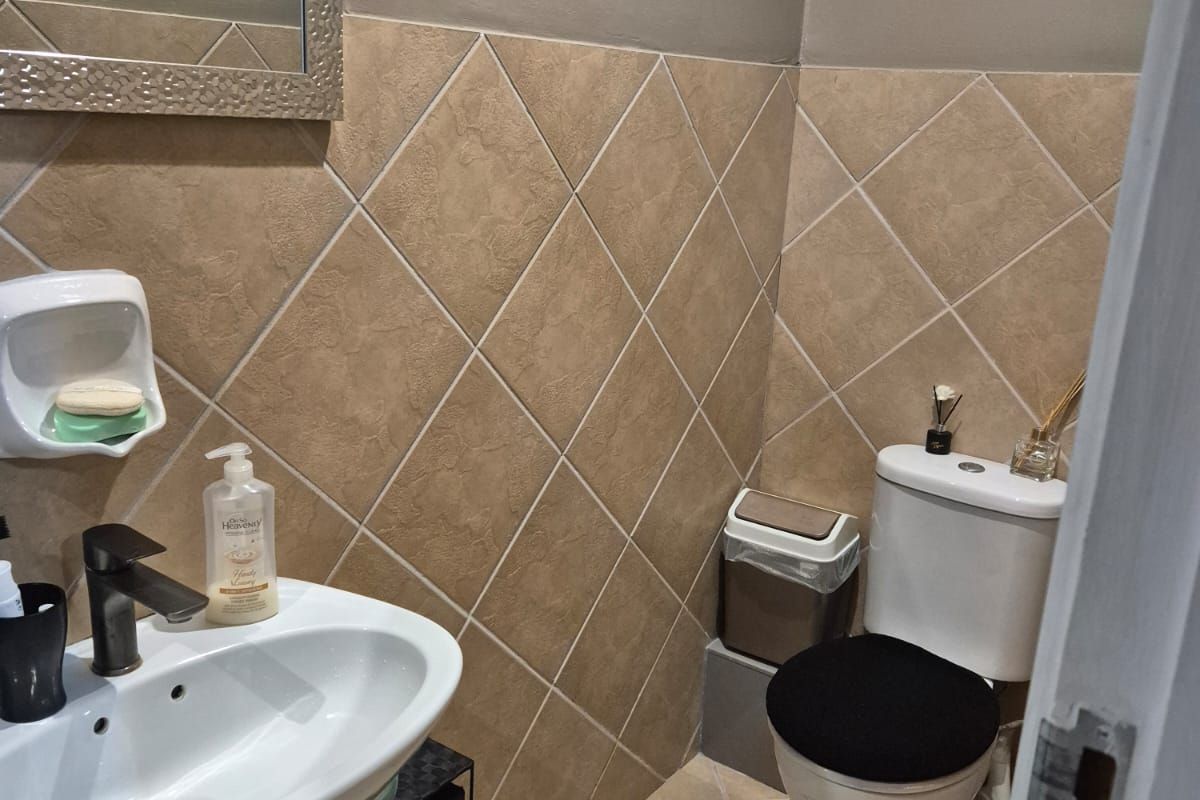 A compact bathroom featuring a pedestal basin, toilet, and neutral diamond-patterned wall tiling.