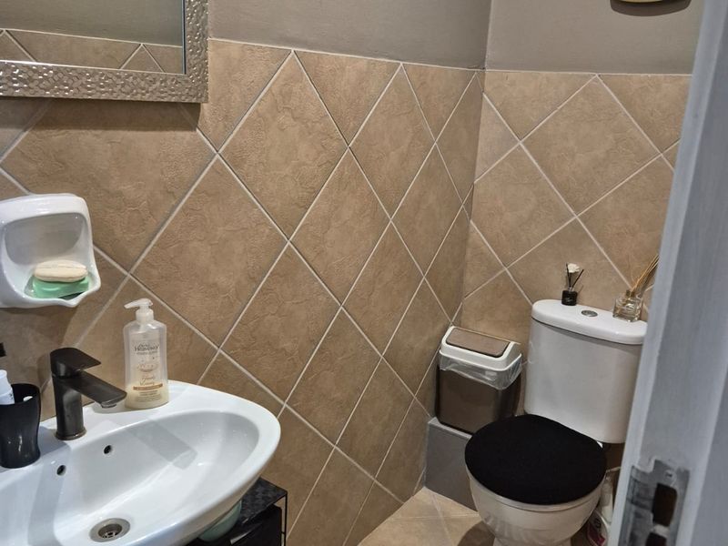 A compact bathroom featuring a pedestal basin, toilet, and neutral diamond-patterned wall tiling.