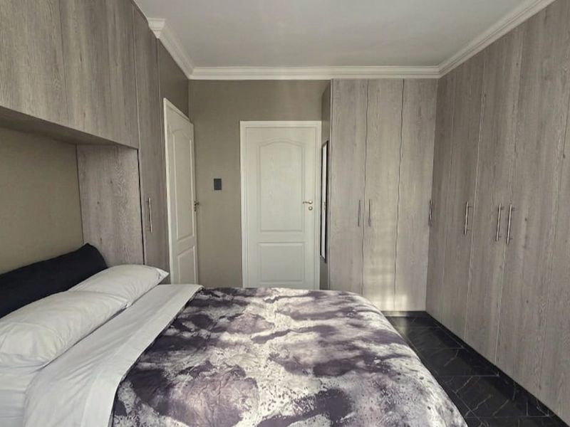 A well-maintained bedroom featuring extensive built-in cabinetry, crown molding, and dark tiled flooring.