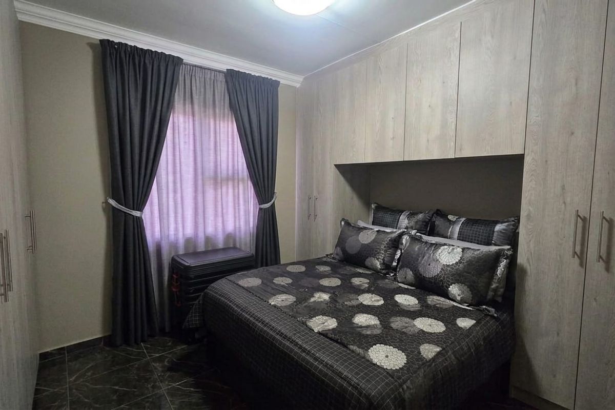 A well-maintained bedroom featuring extensive built-in cupboards, tiled flooring, and decorative cornice detailing.