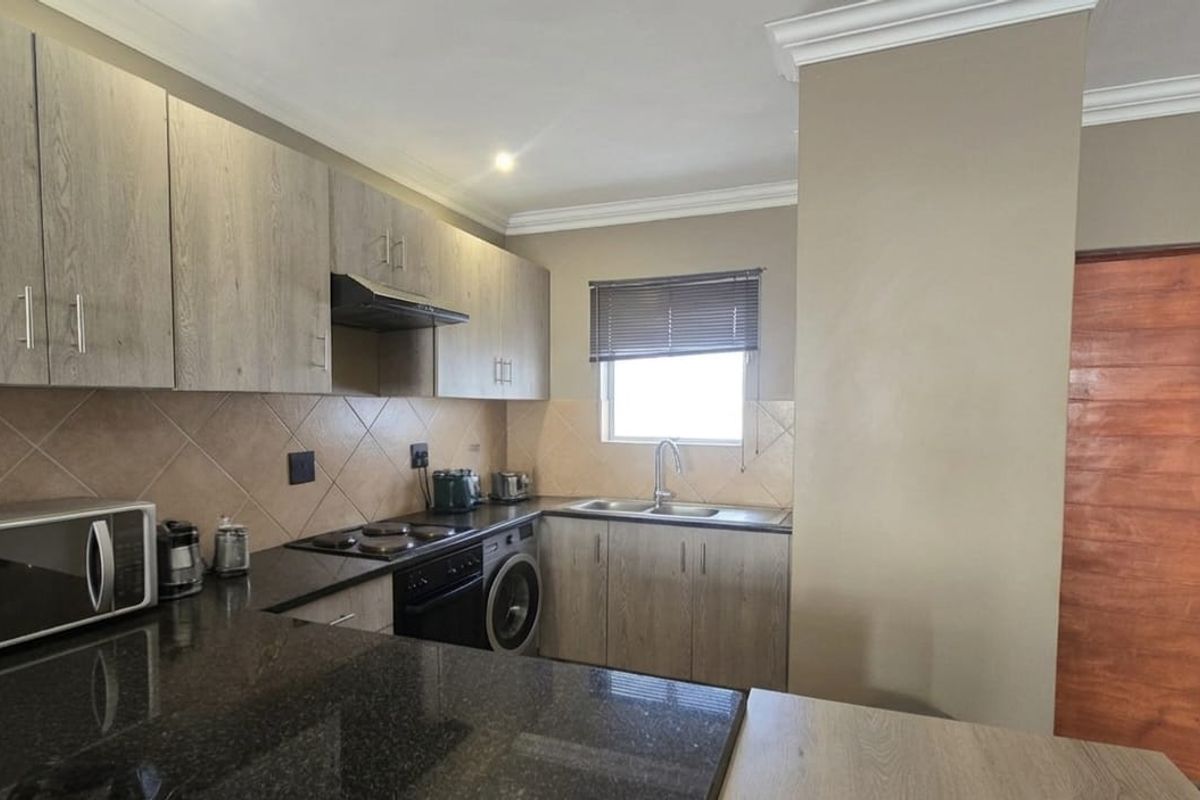 Modern kitchen featuring granite countertops, built-in cabinetry, integrated oven and hob, and a tiled backsplash with a functional layout.