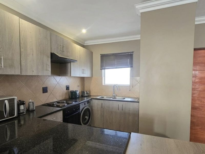 Modern kitchen featuring granite countertops, built-in cabinetry, integrated oven and hob, and a tiled backsplash with a functional layout.