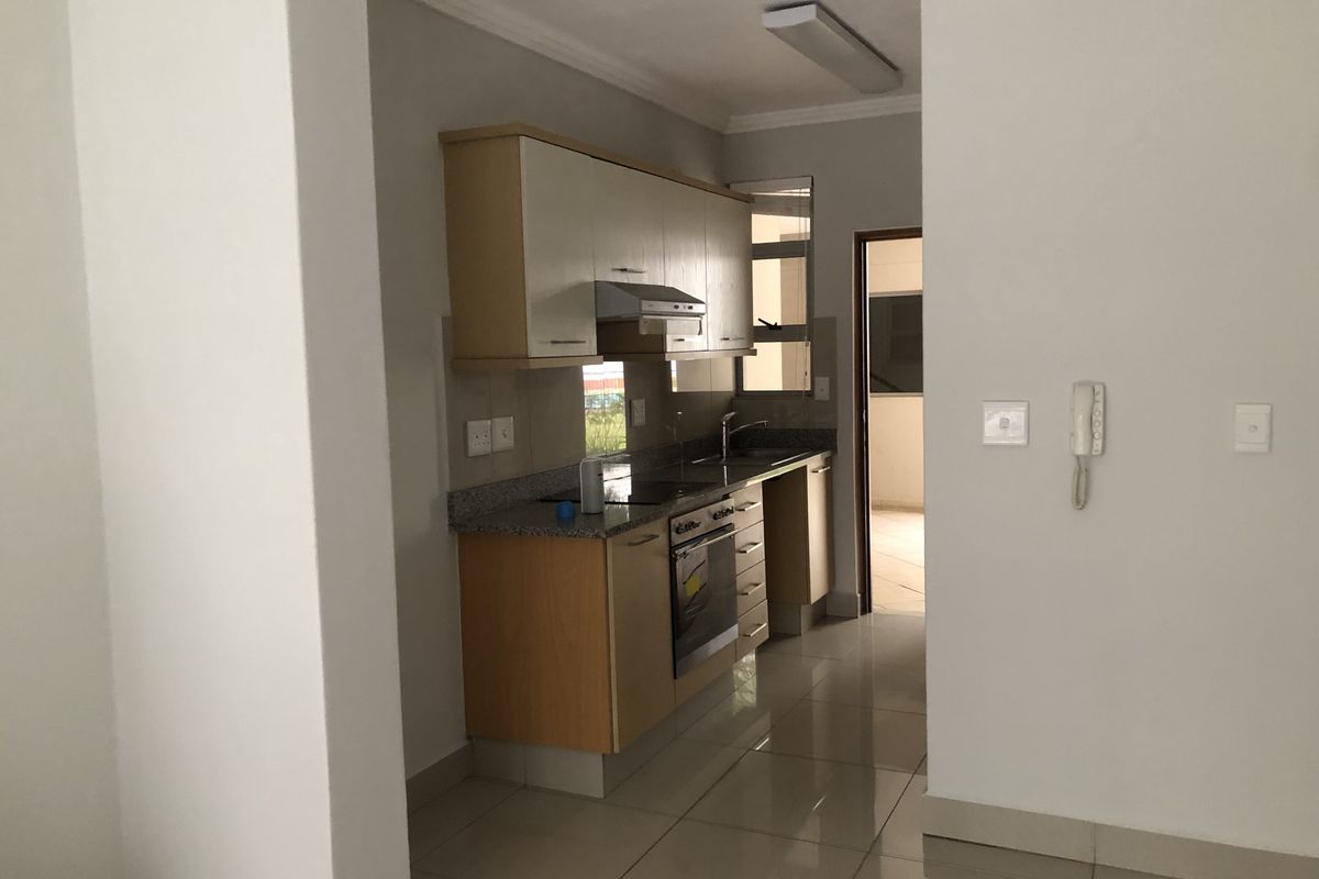 A compact, functional kitchen featuring light wood cabinetry, granite countertops, built-in oven and hob, and tiled flooring, presented in a clean, vacant state.