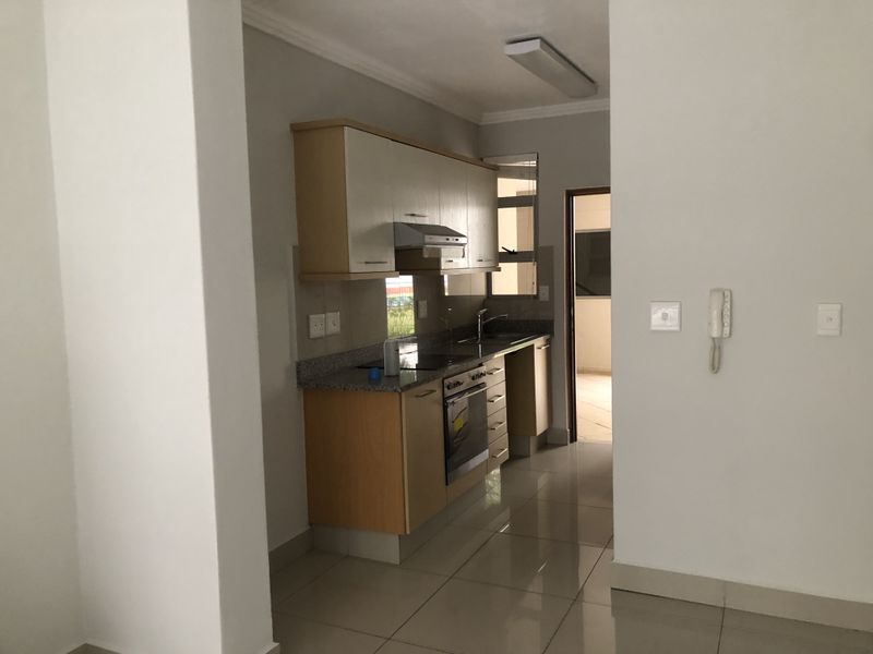 A compact, functional kitchen featuring light wood cabinetry, granite countertops, built-in oven and hob, and tiled flooring, presented in a clean, vacant state.