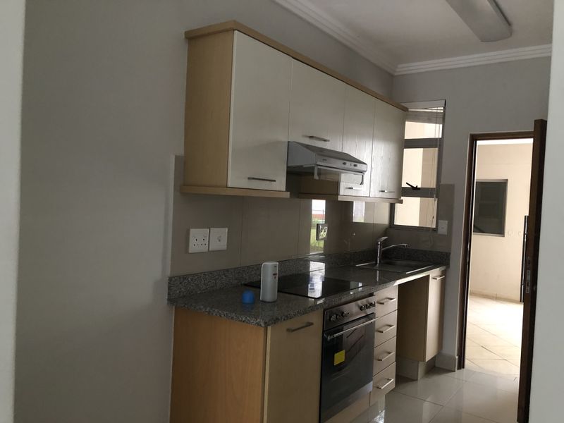 A compact kitchen featuring built-in cabinetry, granite countertops, an electric hob, oven, extractor fan, and a stainless steel sink with tiled flooring.
