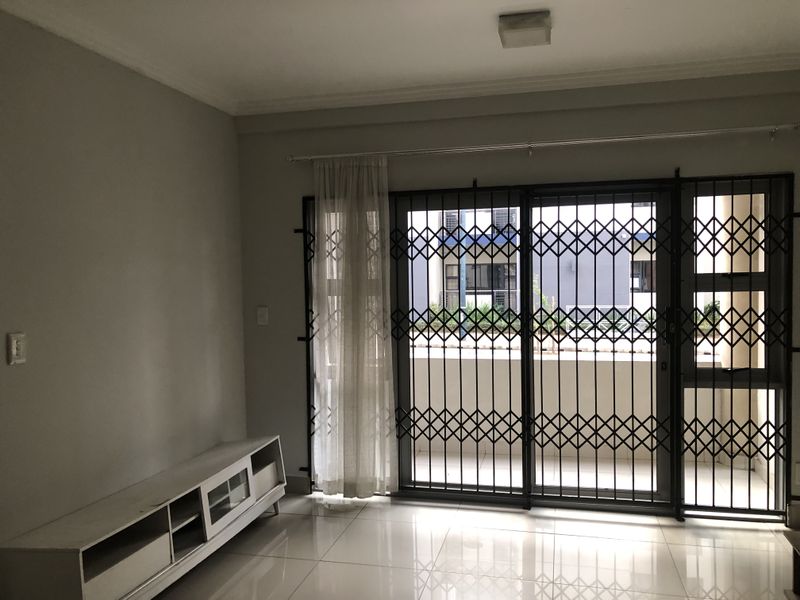 A bright, empty living room featuring tiled flooring and a large sliding glass door with a security gate leading to an outdoor area.