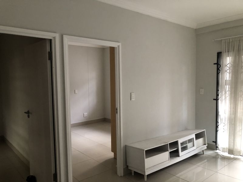 A bright living area featuring neutral tiled flooring, coved ceilings, and direct access to an adjacent room through a doorway.