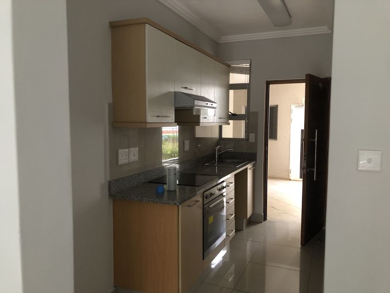 A functional kitchen featuring built-in cabinetry, granite countertops, an electric hob, oven, and extractor fan, with tiled flooring and direct access to an adjacent area.