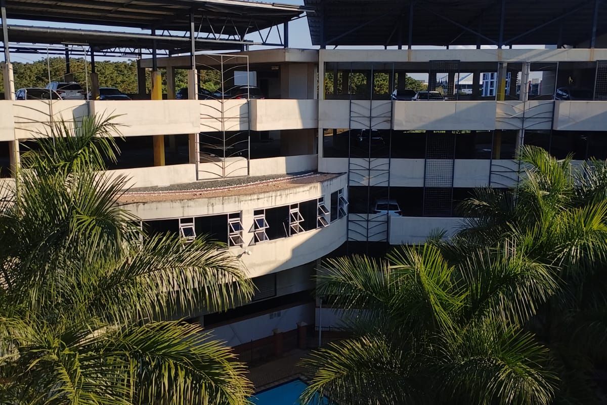 Elevated view of the apartment complex featuring a swimming pool and a multi-level parking structure with metal roofing.