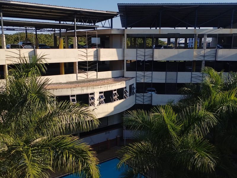 Elevated view of the apartment complex featuring a swimming pool and a multi-level parking structure with metal roofing.