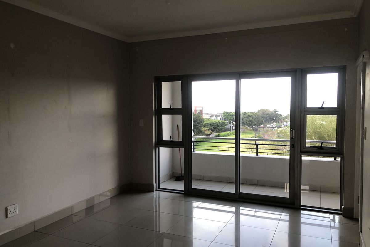 An empty living room featuring tiled flooring and a large sliding glass door providing access to a balcony with exterior views.