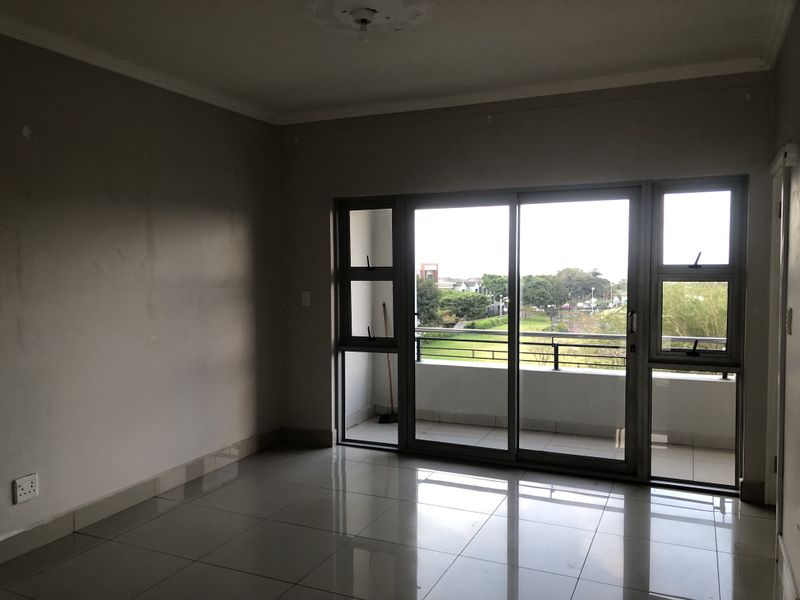 An empty living room featuring tiled flooring and a large sliding glass door providing access to a balcony with exterior views.