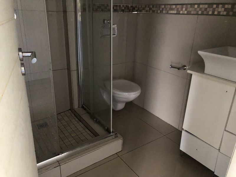 A compact bathroom featuring a glass-enclosed shower, wall-mounted toilet, and a vessel sink set on a vanity cabinet with tiled finishes.