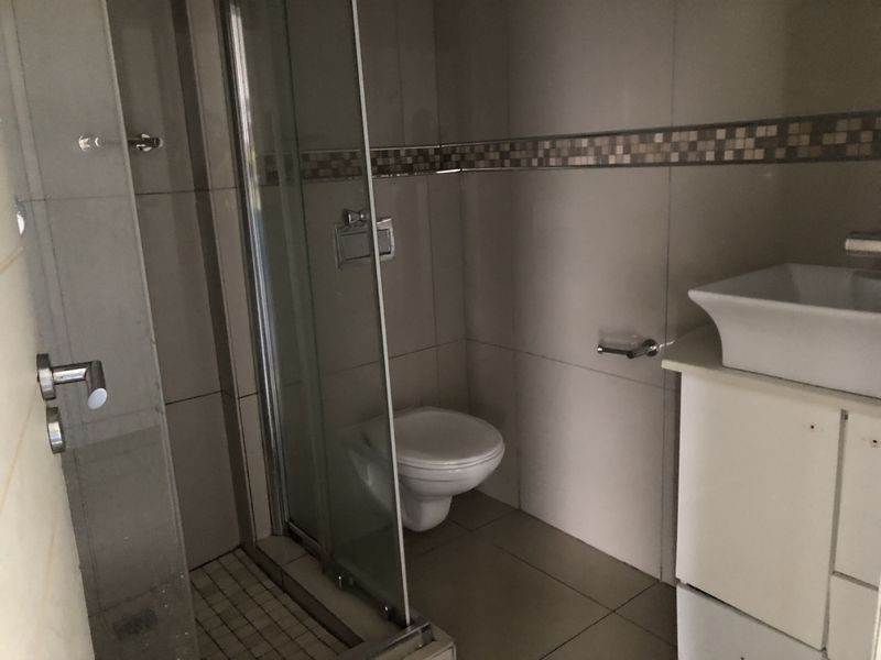 A functional bathroom featuring a glass-enclosed shower, wall-mounted toilet, and a vessel sink vanity with tiled finishes throughout.
