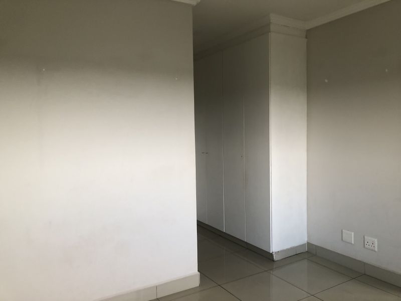 An empty bedroom featuring neutral walls, tiled flooring, and built-in cupboards with clean lines.