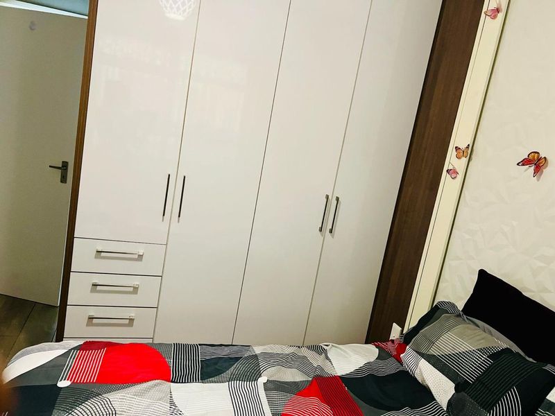 A bedroom featuring a modern, white high-gloss built-in wardrobe with integrated drawer storage.