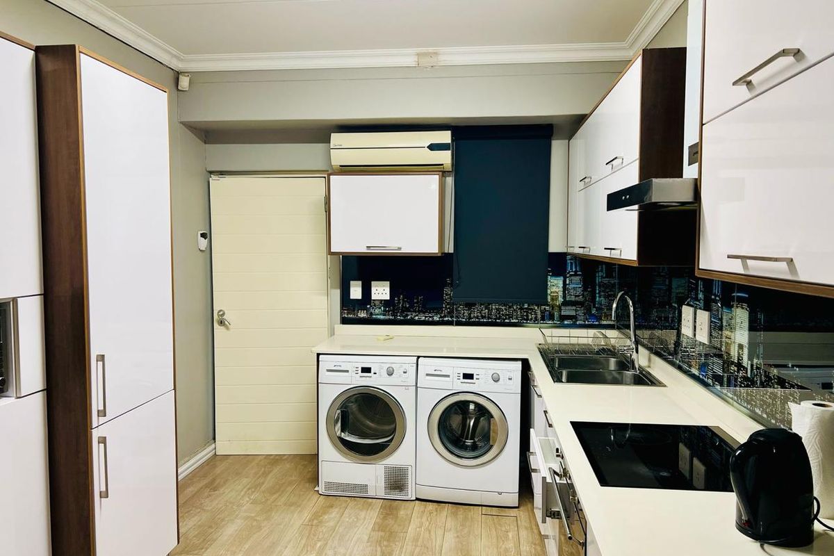 Modern kitchen featuring white cabinetry, stone countertops, induction cooktop, extractor fan, and integrated laundry appliances with a city-themed splashback.