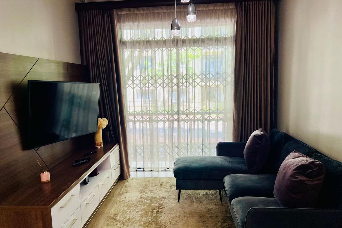 A cozy living room featuring a built-in media console, large window with security gate, and modern pendant lighting.