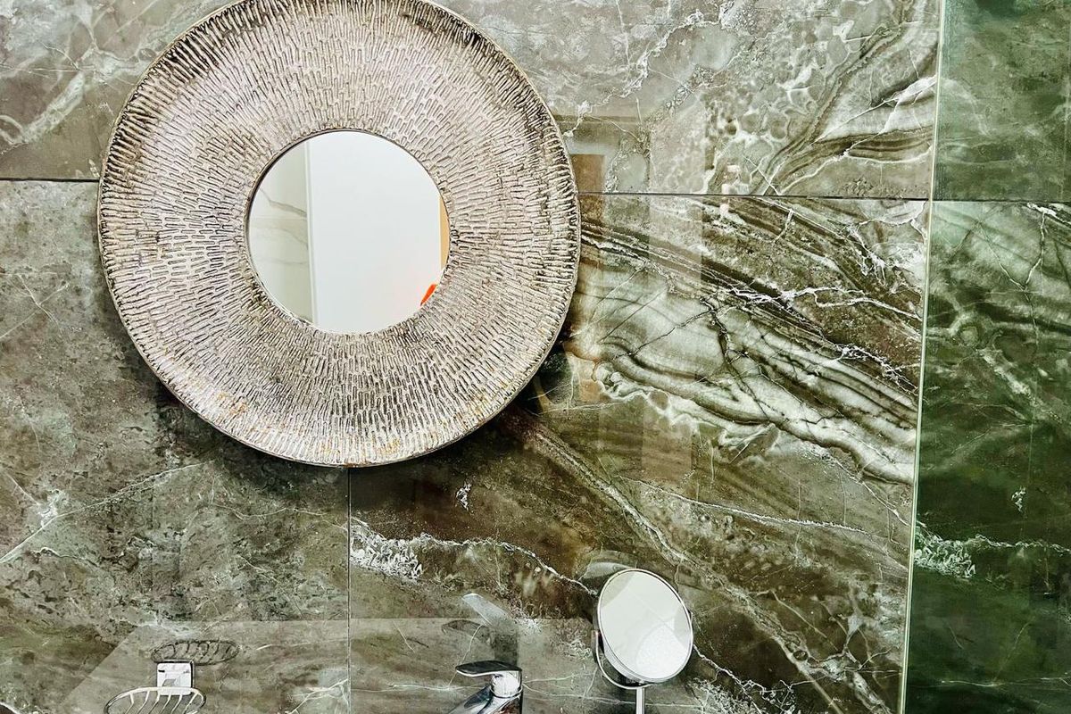A modern bathroom featuring high-end large format marble-look wall tiles, a sleek chrome basin mixer, and a glass shower screen.